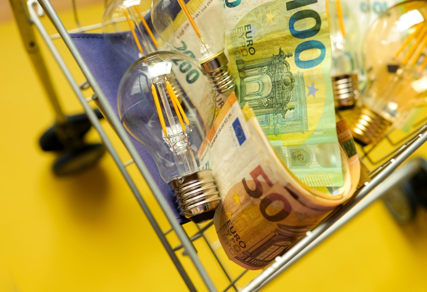 A shopping cart full of light bulbs and euros on a yellow background. Representing Success in The Electrical Sector.